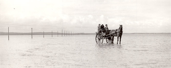 A mail cart is being driven across a shoreline bound for Holy Island (POST 118/854)